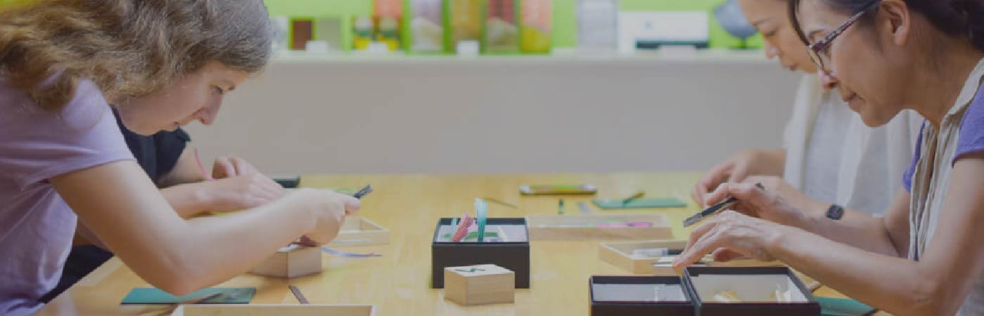 Background image showing touristing doing straw craft on a table