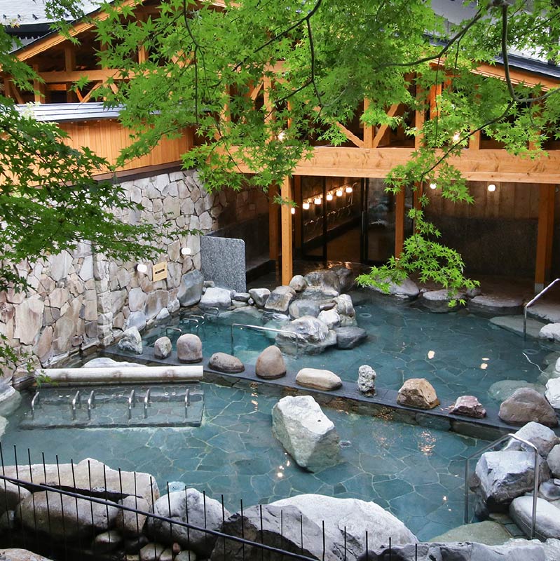 Goshonoyu Onsen's open and expansive outdoor baths. Maple tree branches hang over the pools.