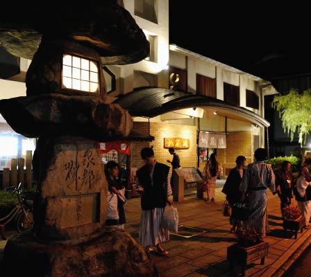 A large group of people in colorful yukata walking and talking around the entrance of Jizoyu Onsen
