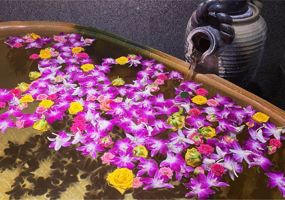 A private ryokan bath, filled to the brim and complete with colorful flowers floating above the water