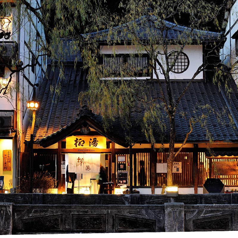 Yanagiyu Onsen exterior, moodily light at twilight with yellow lanters. A willow ('Yanagi' in Japanese) covers the entrance to the onsen.