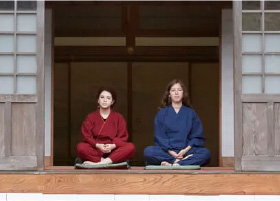 Two foreign woman sitting in pentive cross-legged poses on the veranda of a temple