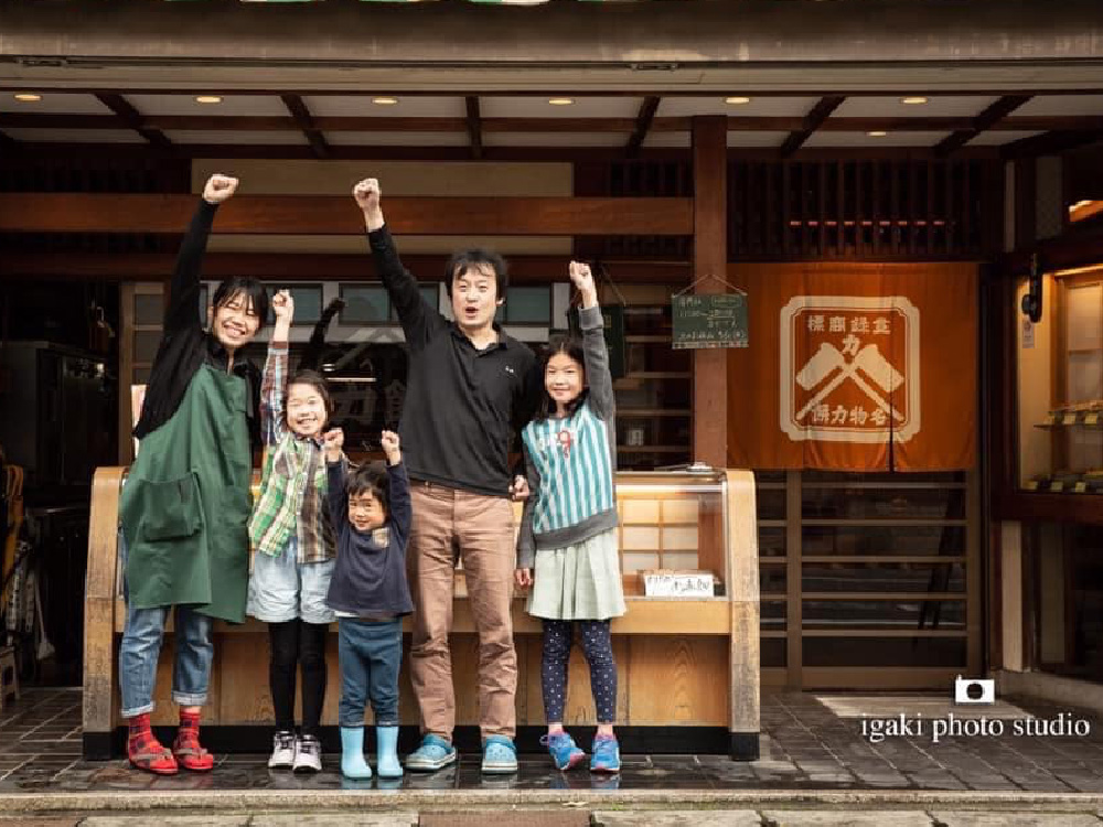 The owners of Chikara Mochi restaurant and their family all raising one of their hands in a fist, as if to say 'power!'. ('Chikara' means power in Japanese, and Mochi is a type of rice cake)