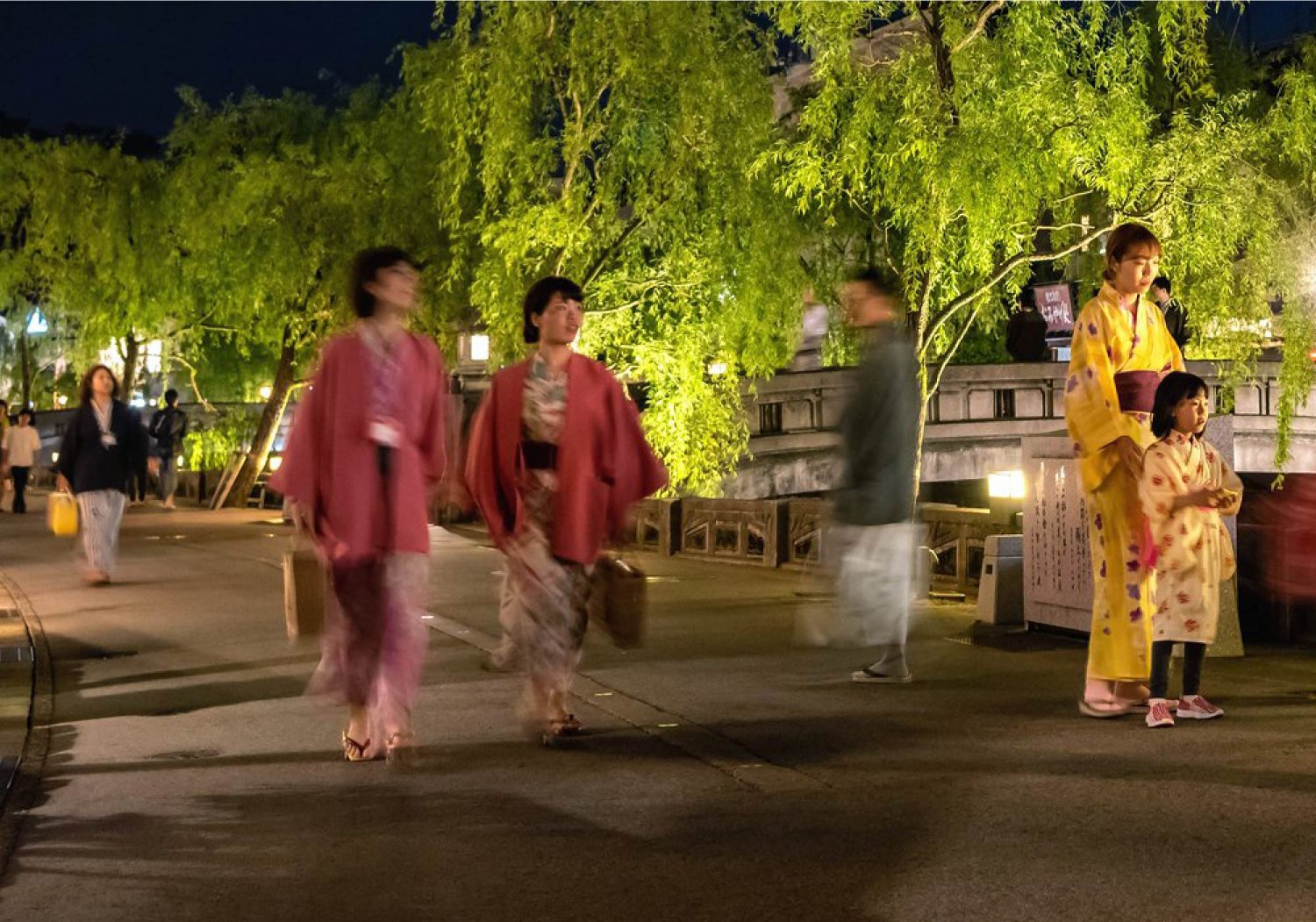People walking the willow-lined streets of Kinosaki Onsen in their colorful Yukata at night