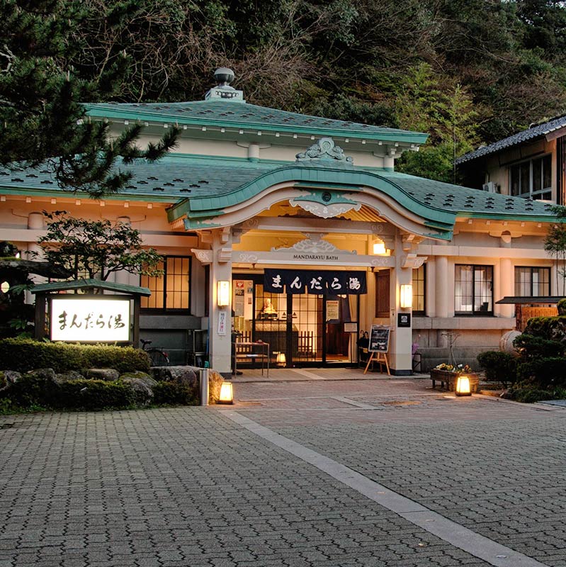 The exterior of Mandara-yu Onsen at twilight, with it's green tiled roof and moody exterior lighting.
