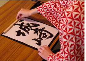 A woman writing 'Kinosaki Onsen' in Japanese characters, in the traditional art of Japanese calligraphy