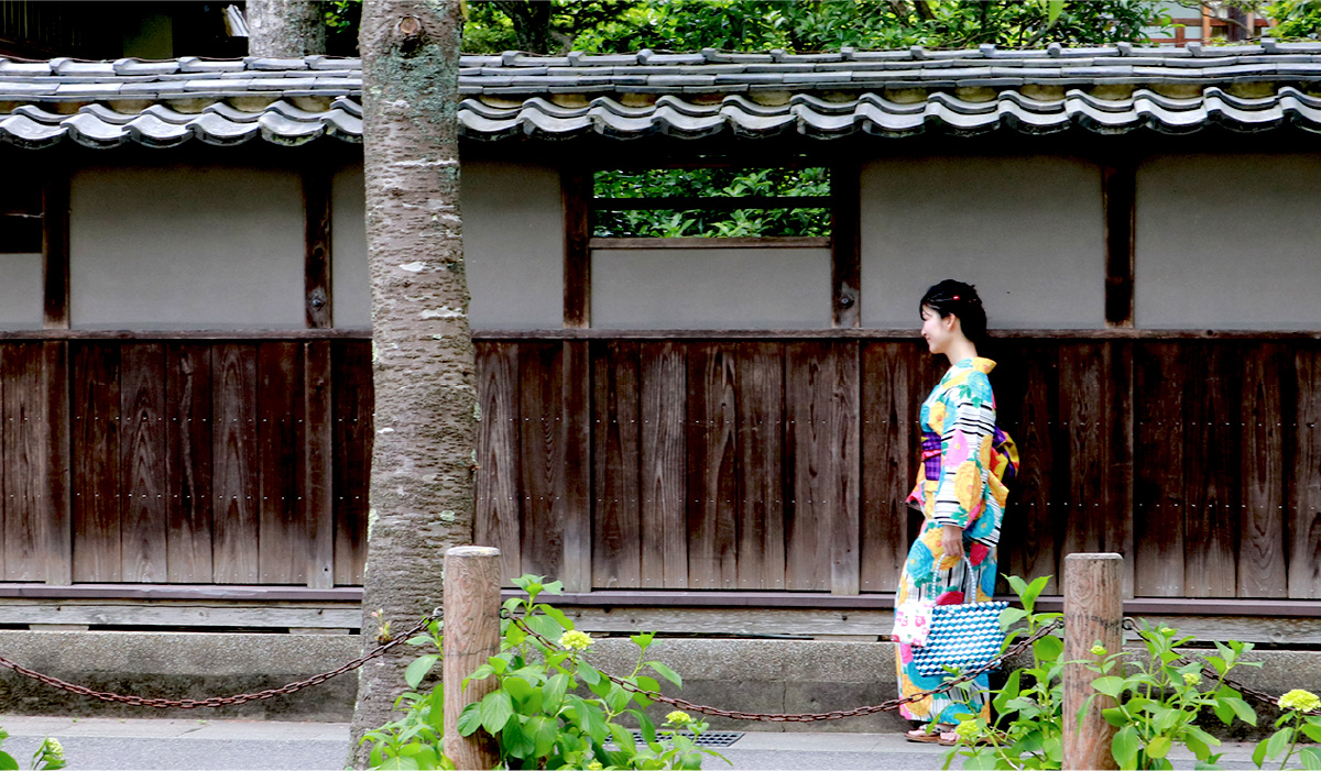 A woman in colorful Yukata strolling past a traditional Japanese manor wall